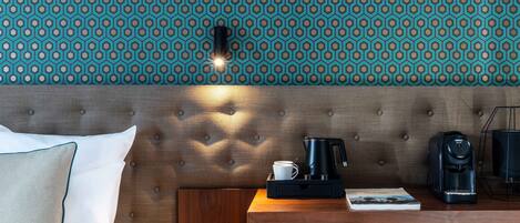 A hotel room with a tufted headboard, a wooden nightstand, a coffee maker, a cup, and a book.