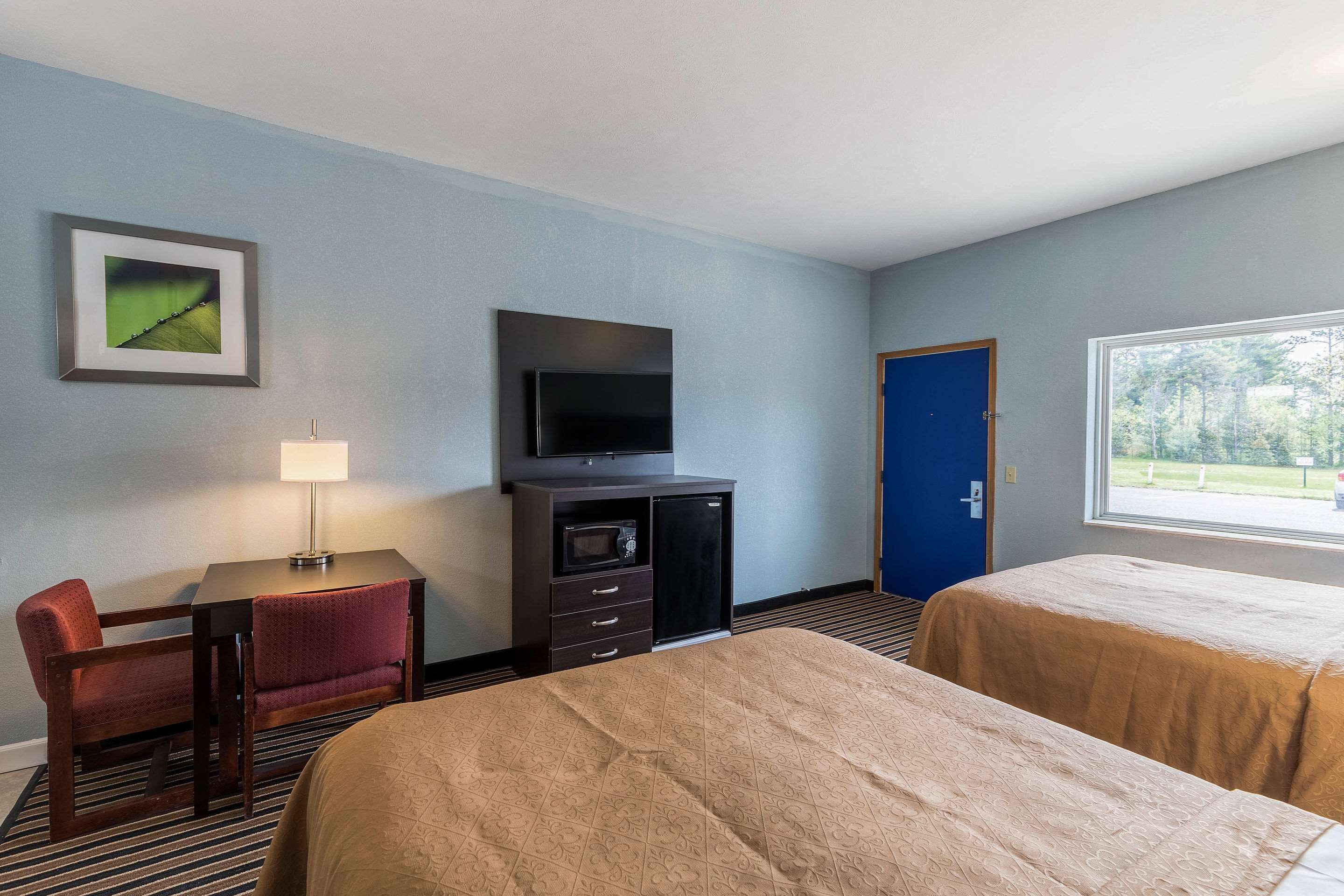 A hotel room with two beds, a desk with a chair, a television, a microwave, and a door.