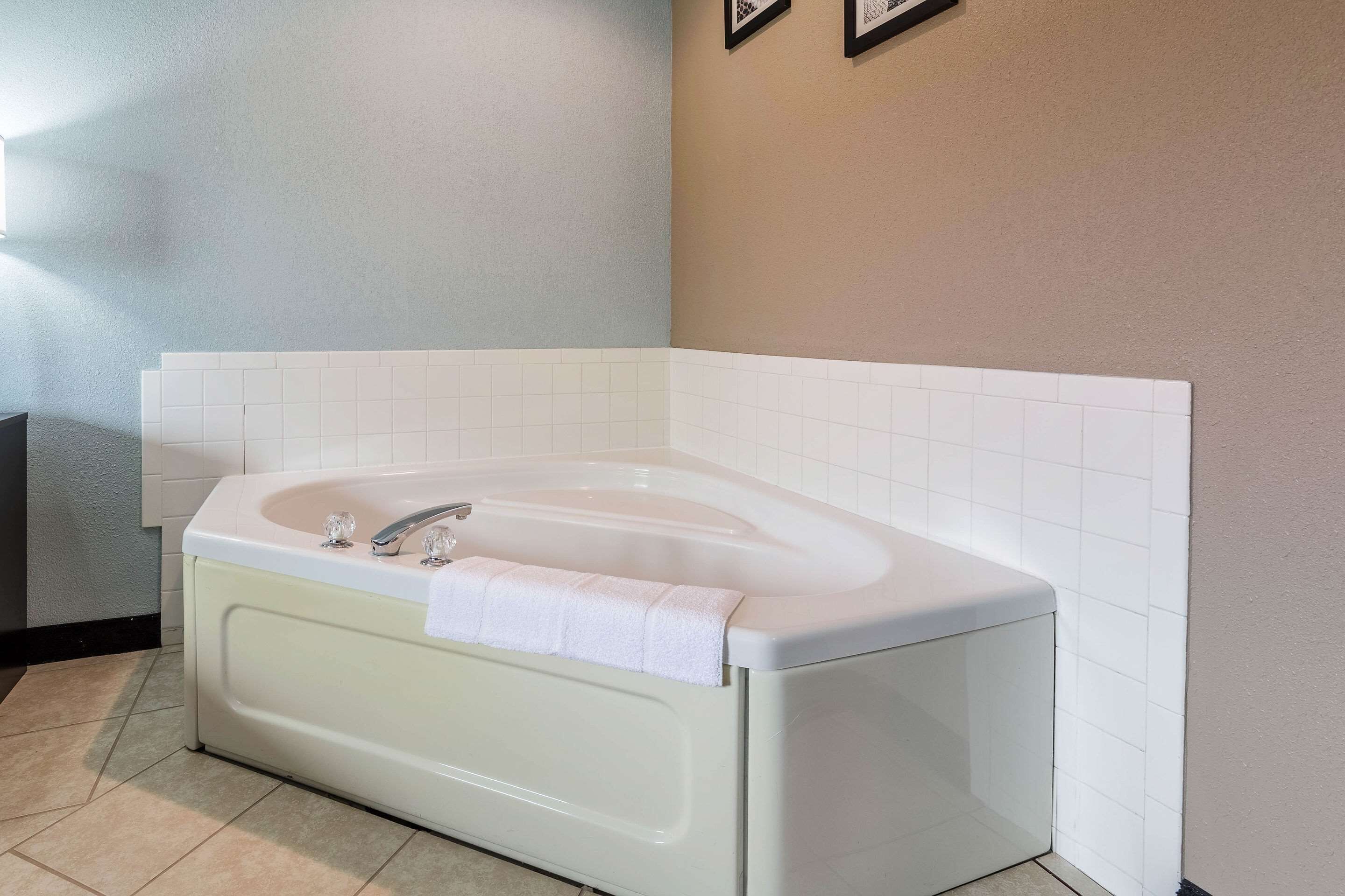 A corner bathroom with a white bathtub, a towel on the edge, and white tiled walls.