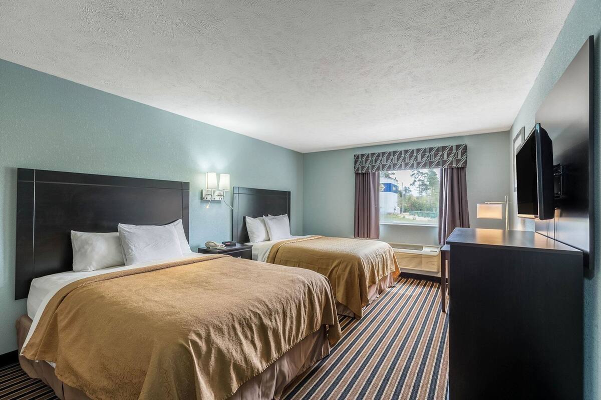 Habitación de hotel con dos camas, televisión de pantalla plana, escritorio y ventana con cortinas.