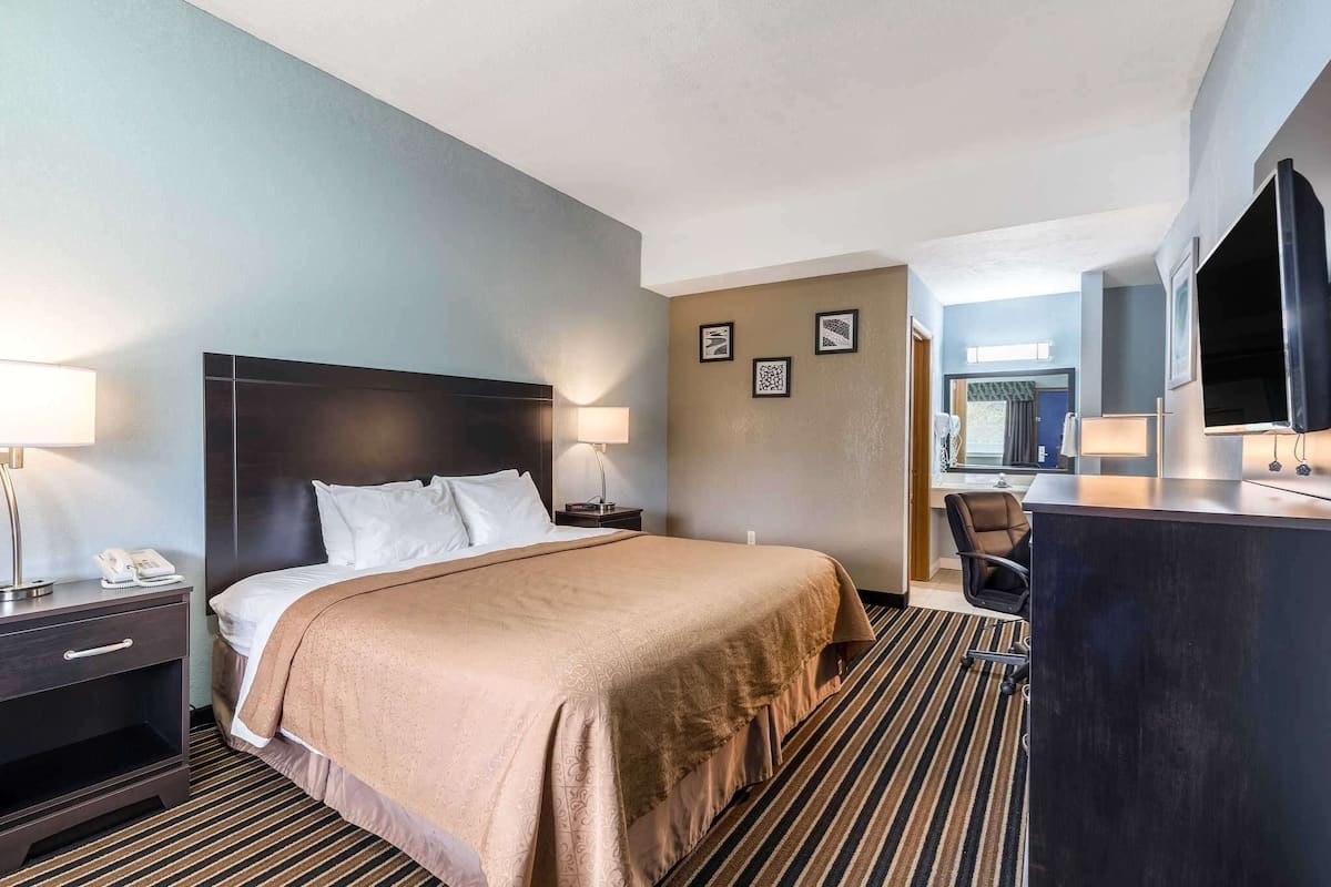 Habitación de hotel con cama, mesita de noche, lámpara y escritorio con silla.