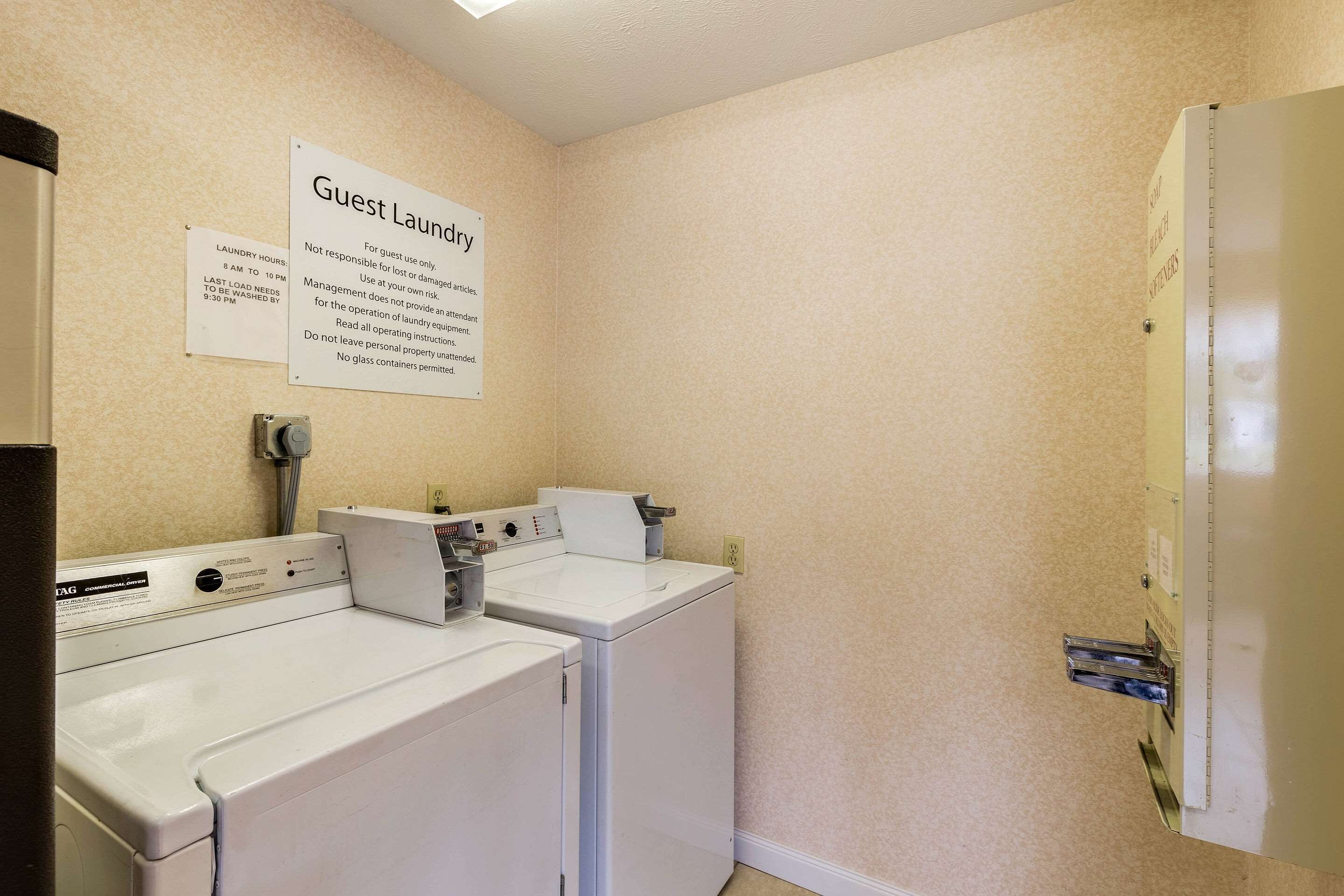 A laundry area with two washers and dryers, a sign indicating guest laundry hours, and a note about glass containers.