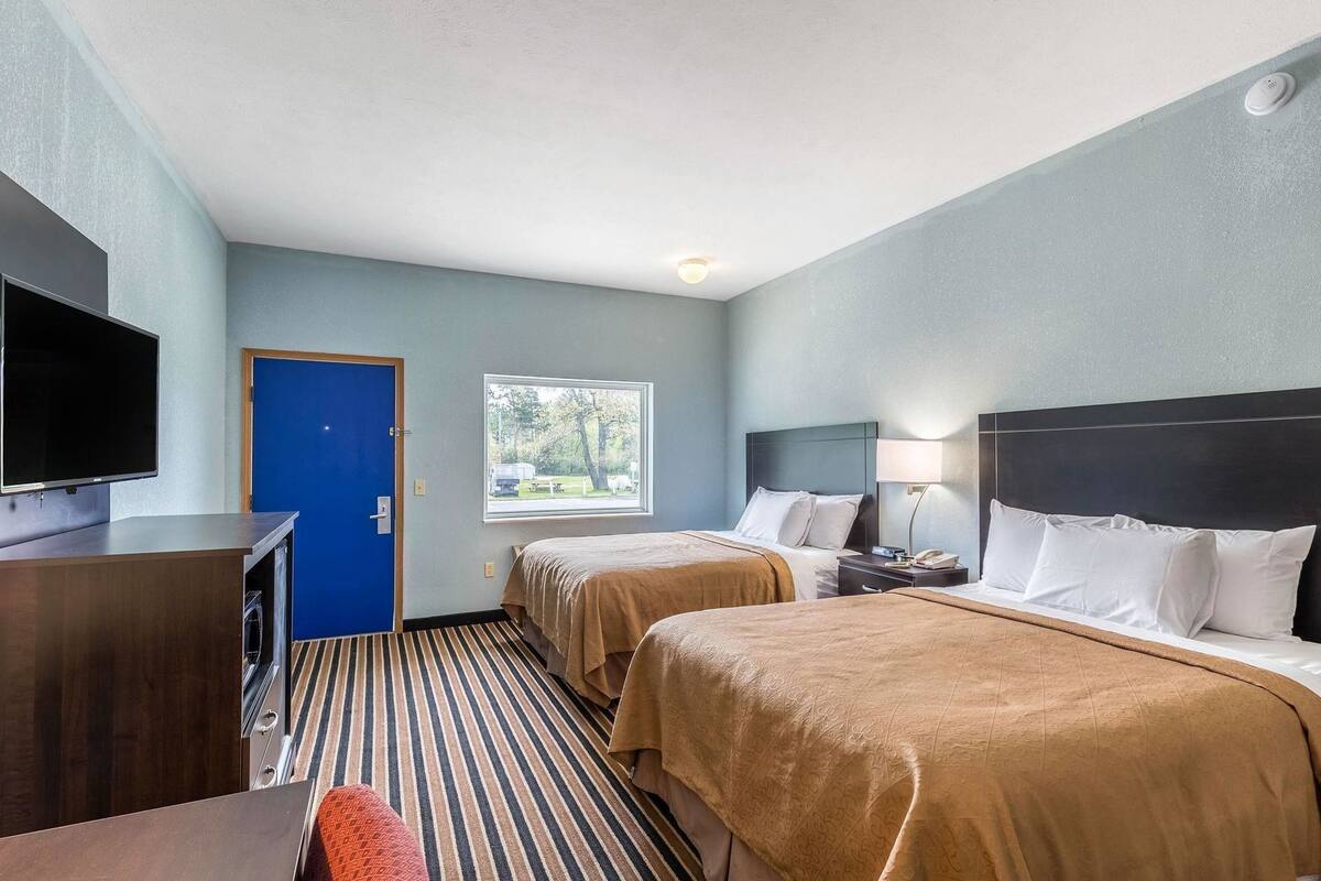 Habitación de hotel con dos camas, televisión, escritorio y ventana con vistas a árboles.