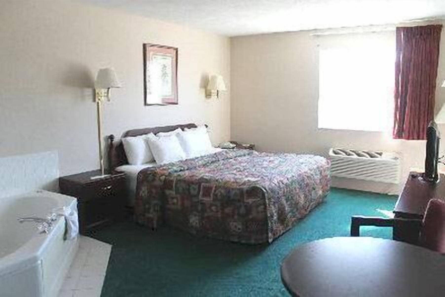 A hotel room with a bed, a desk, a chair, a window with curtains, and a radiator.