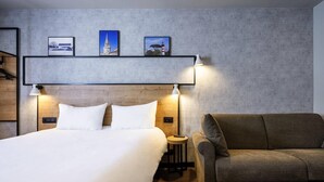 Ein Hotelzimmer mit einem Bett, einer Couch, einem Nachttisch und drei gerahmten Bildern an der Wand.