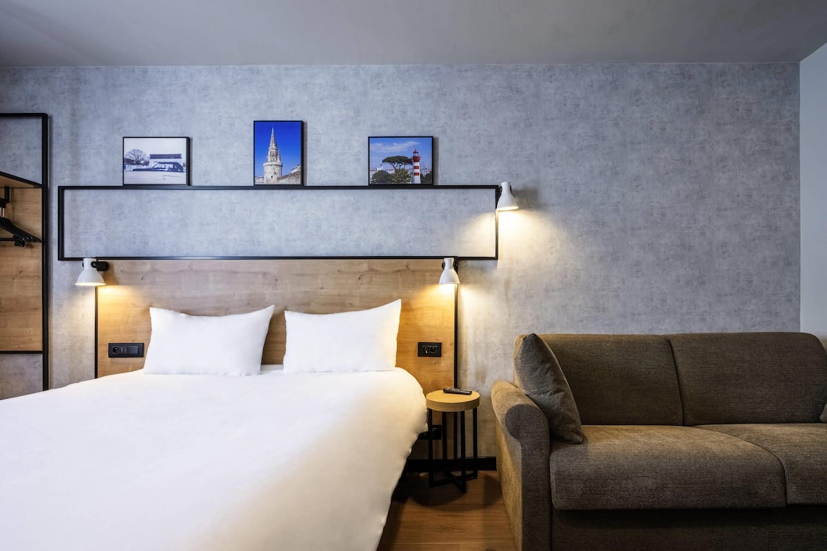 Une chambre dâhĂŽtel avec un lit, un canapĂ©, une table de chevet et trois tableaux encadrĂ©s accrochĂ©s au mur.