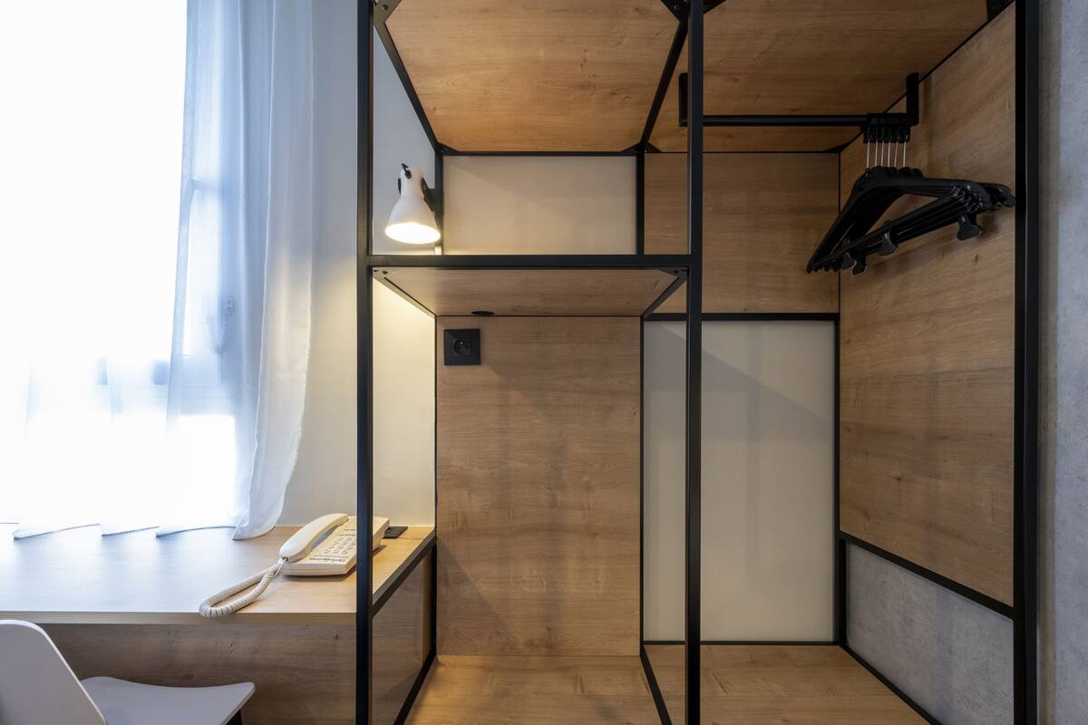 A compact room with a wooden desk, a telephone, a lamp, and a coat rack.