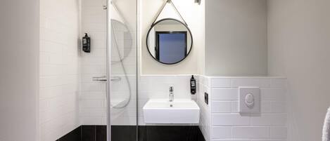 A modern bathroom with a glass-enclosed shower, a white sink, and a black-tiled floor.