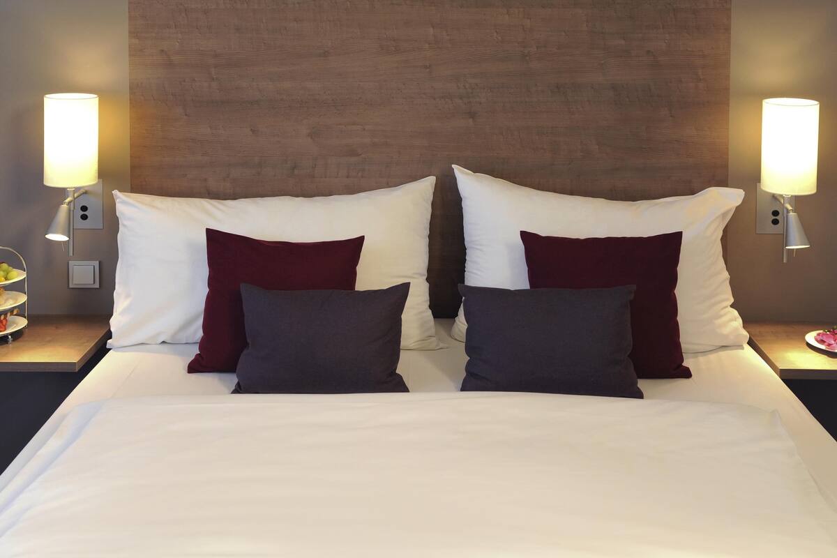 A hotel room with a large bed, two bedside tables, two wall-mounted lamps, and a wooden headboard.
