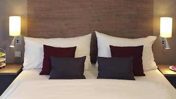 Habitación de hotel con una cama grande, dos mesitas de noche, un cabecero de madera y lámparas fijadas a la pared.