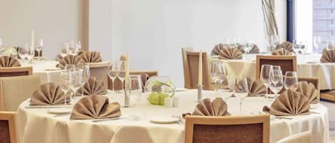 Un comedor con mesas redondas, sillas y un gran ventanal con vistas a un edificio.