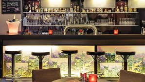 A bar area with a cityscape view, bar stools, and a variety of bottles and glasses. - Mercure Hotel Frankfurt Eschborn Ost (Eschborn)