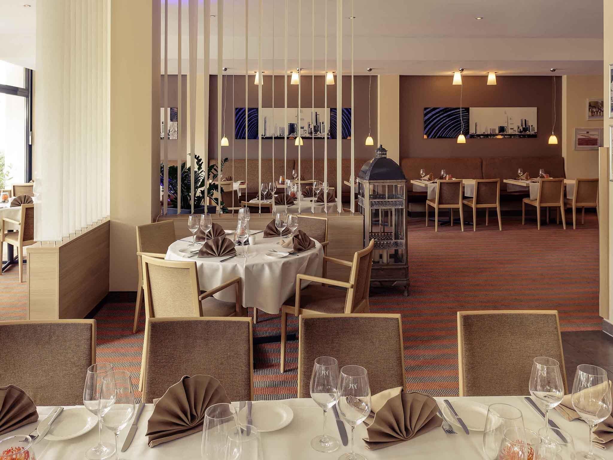 A dining area with tables set for service, a cityscape mural, and a decorative lantern.
