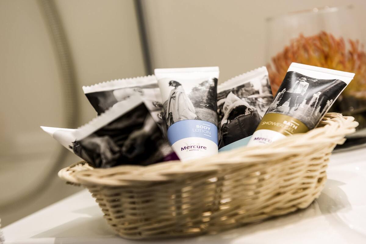 A wicker basket containing toiletries including a body lotion, a shower gel, and a Mercure hotel-branded item.