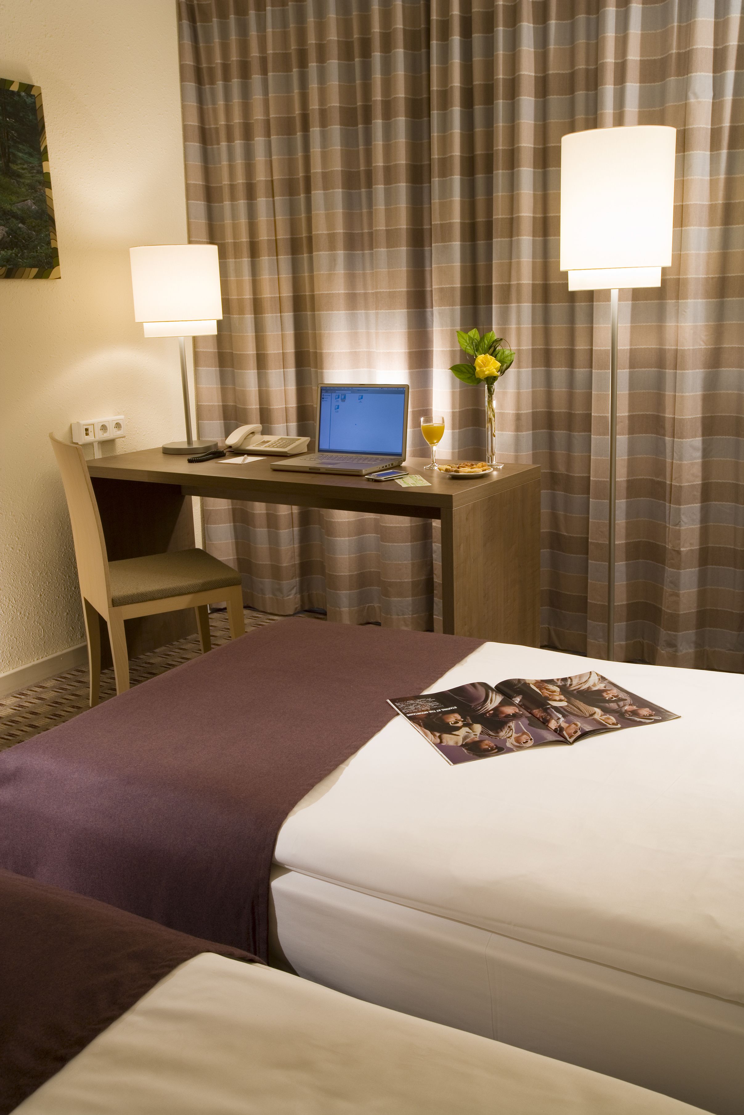 Ein Hotelzimmer mit zwei Betten, einem Schreibtisch mit Laptop, Telefon und einer Vase mit Blumen.