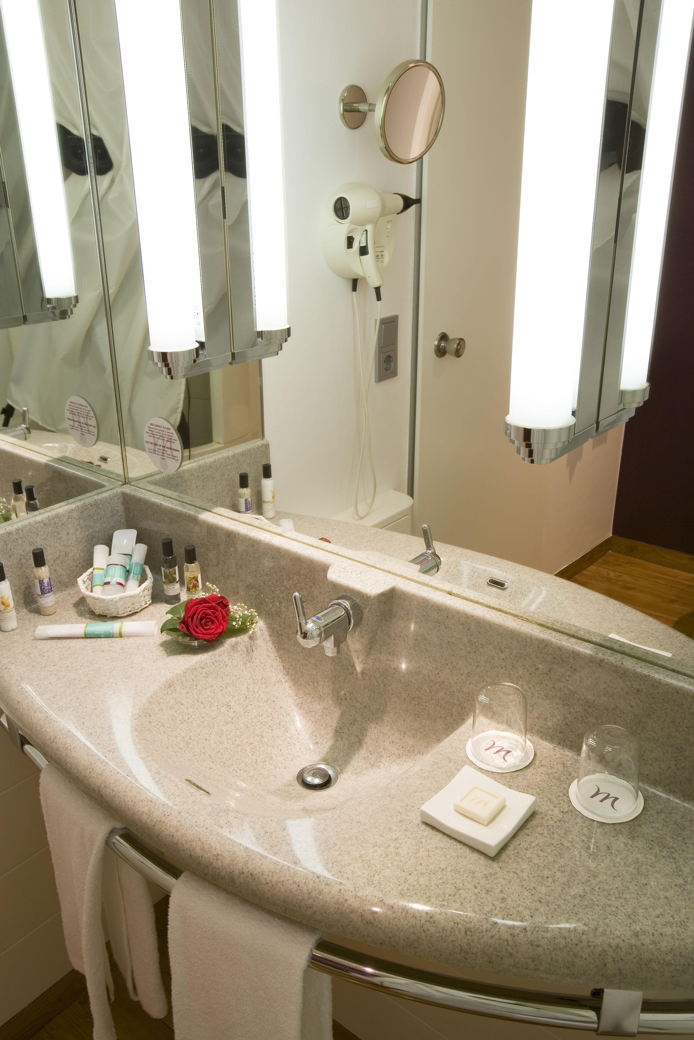 A bathroom with a large sink, mirrors, a hairdryer, and toiletries.