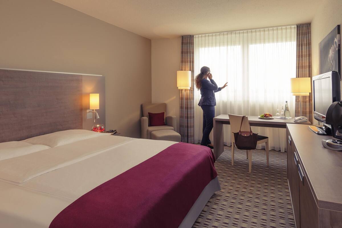 A hotel room with a large bed, a desk with a chair, a television, and a window with curtains.