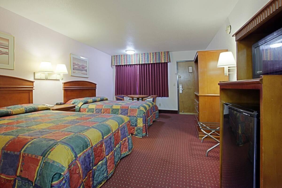 Une chambre d’hôtel avec deux lits, un bureau, une télévision et une porte.