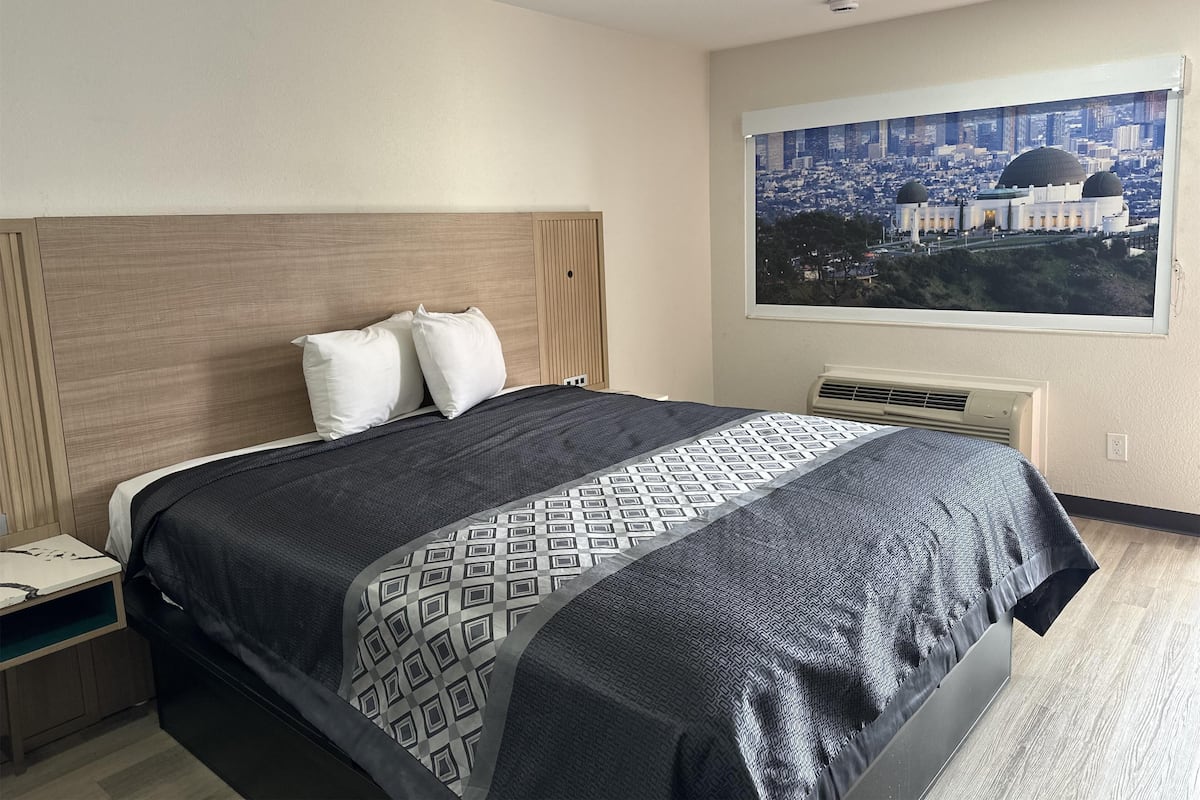 Une chambre d’hôtel comprenant un lit, une table de chevet, une fenêtre donnant sur la ville et un climatiseur fixé au mur.