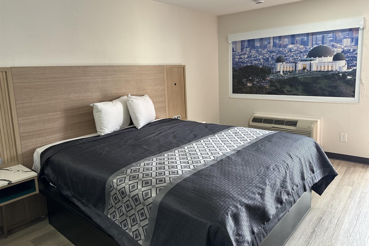 Une chambre d’hôtel comprenant un lit, une table de chevet, une fenêtre donnant sur le paysage urbain et un appareil de climatisation.