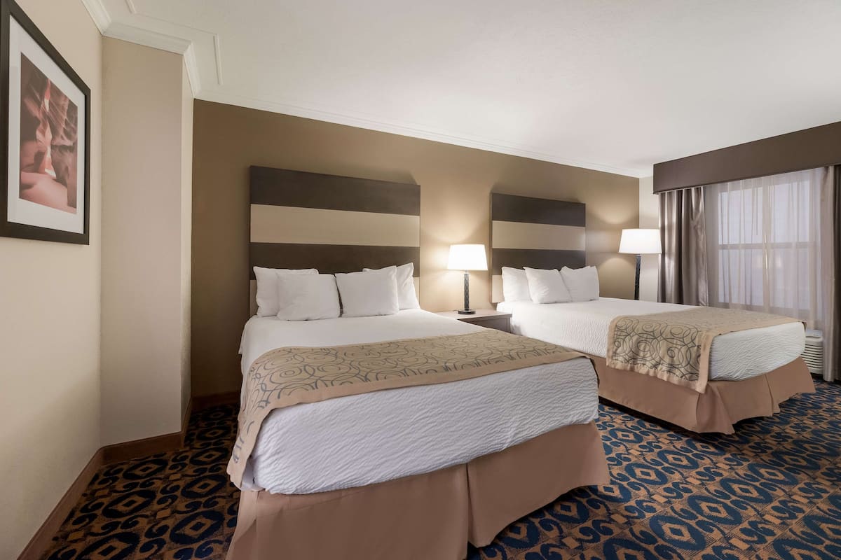 A hotel room with two beds, a patterned carpet, and a framed picture on the wall.