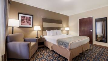 A hotel room with a bed, a chair, a nightstand, a lamp, a framed picture on the wall, and a patterned carpet.