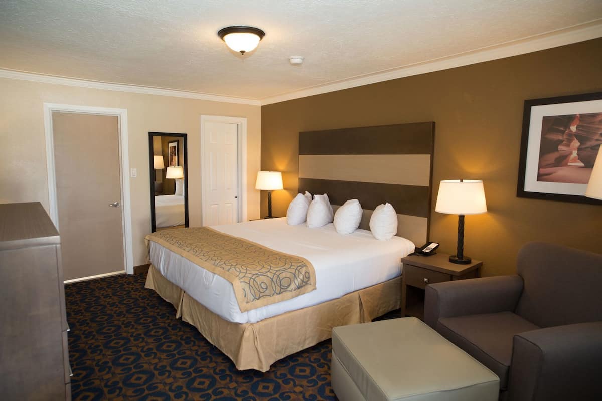 A hotel room with a bed, bedside lamps, a chair, a desk, and a carpeted floor.