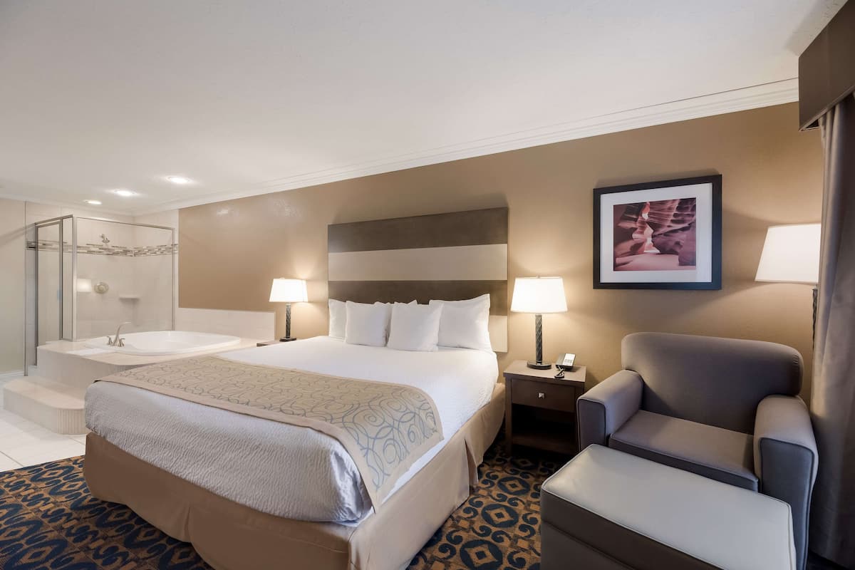 A hotel room with a large bed, a shower, a chair, and a nightstand with a lamp.