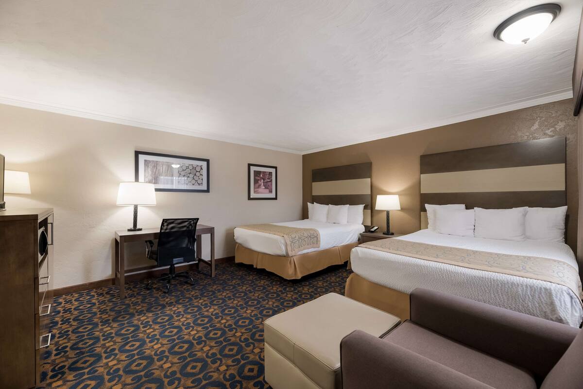 A hotel room with two beds, a desk, a chair, and a sofa.