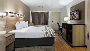 Una habitación de hotel con cama, mesita de noche, lámpara, televisor y un escritorio con silla.