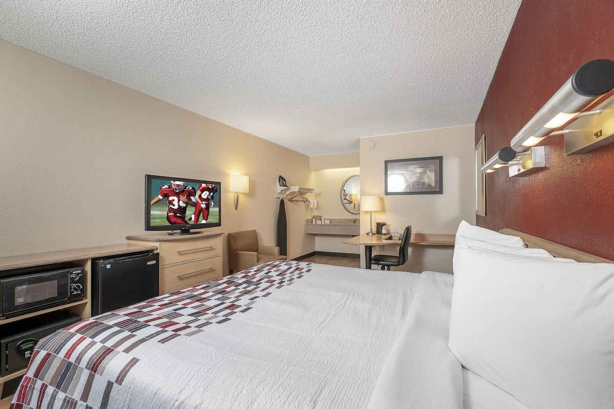 A hotel room with a bed, a desk, a chair, a television, and a microwave.