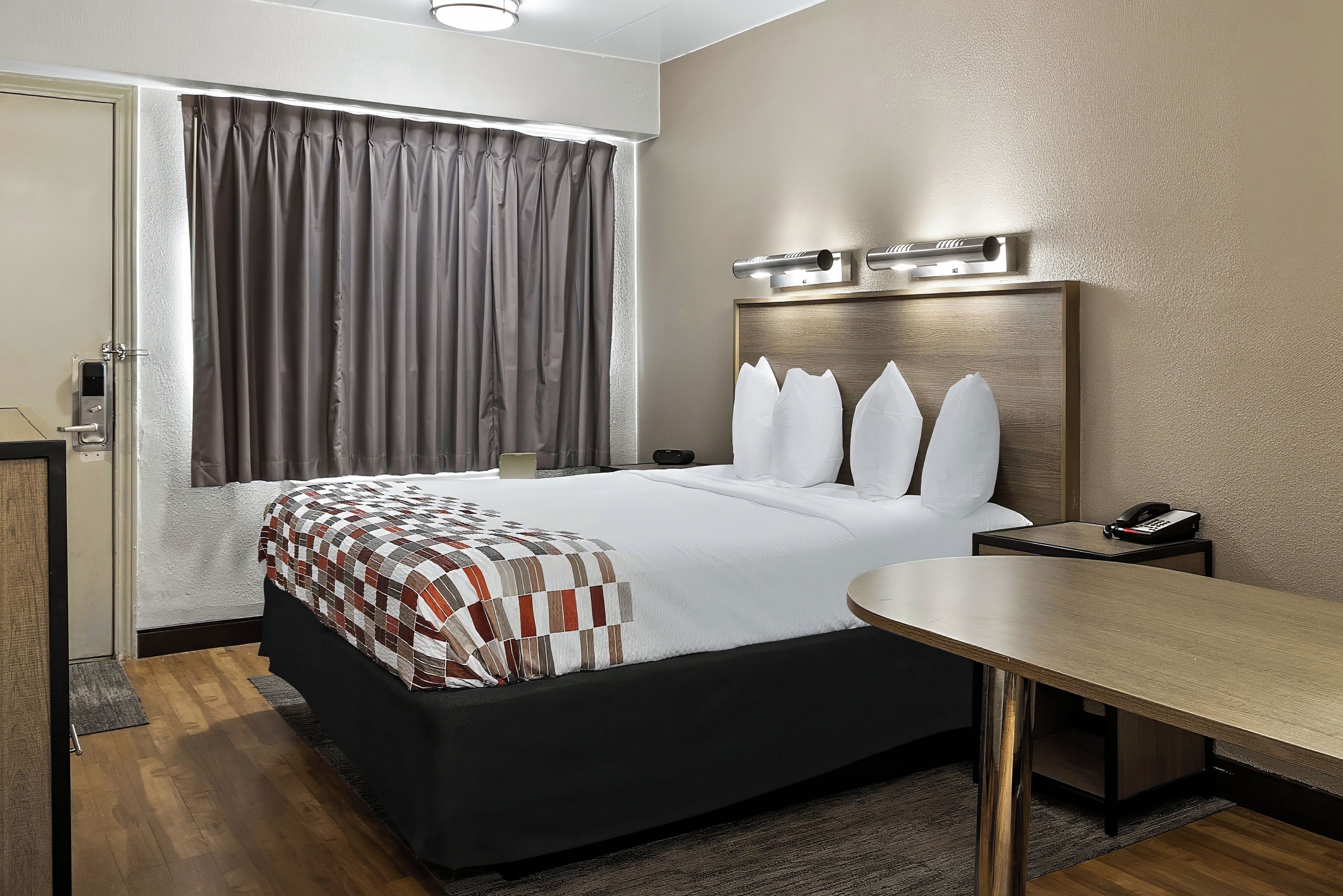Una habitación de hotel con cama, escritorio, teléfono y ventana con cortinas.