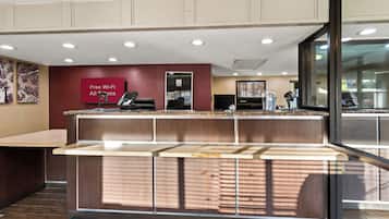 A reception area with a counter, a 'Free Wi-Fi All Rooms' sign, a 'No Smoking' sign, and a view of the outside through a large window.