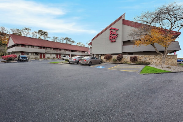 A Red Roof Inn with a parking lot, a building with a red roof, and a tree with autumn leaves.