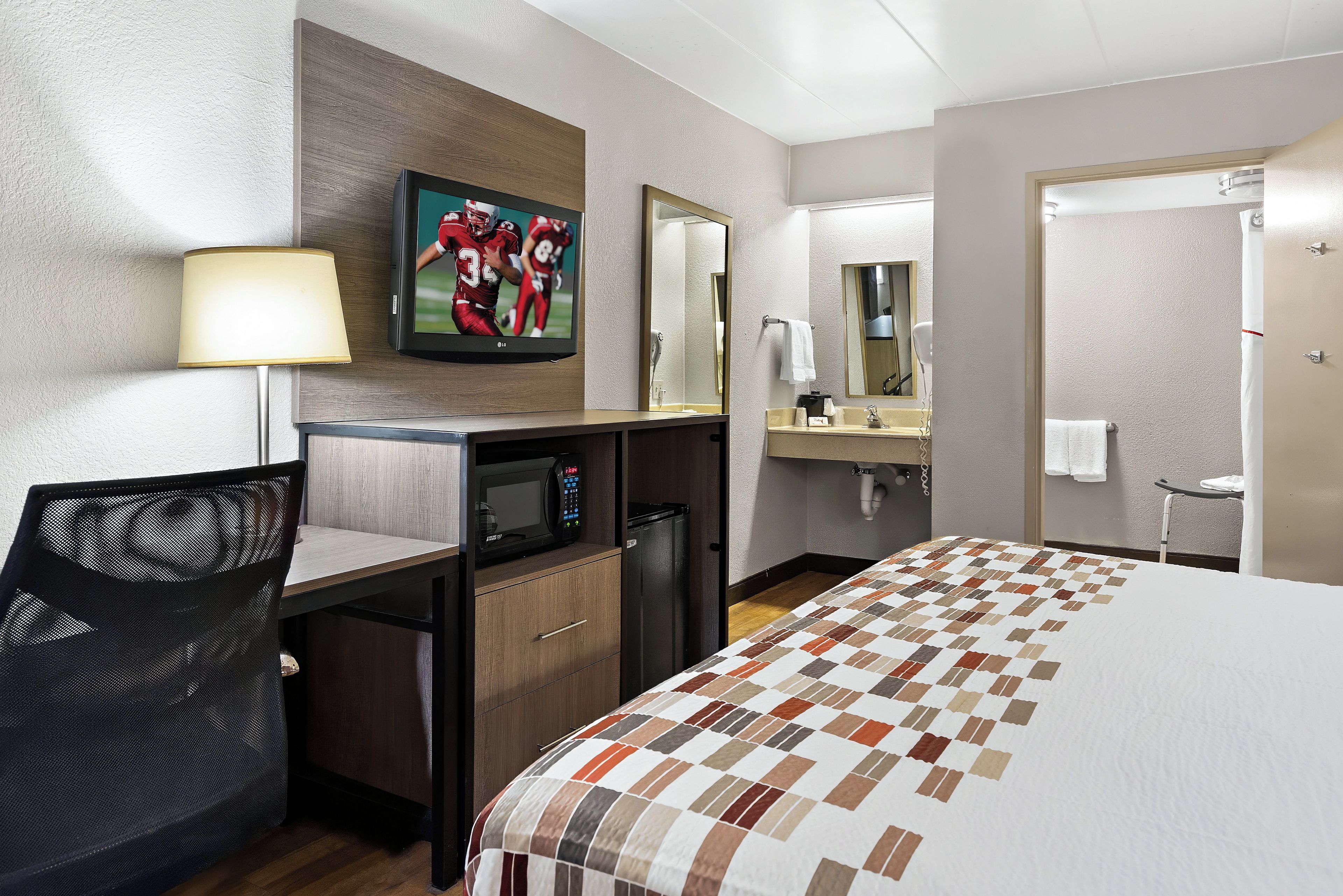 Ein Hotelzimmer mit Bett, Schreibtisch, Stuhl, Fernseher, Mikrowelle und Badezimmer.