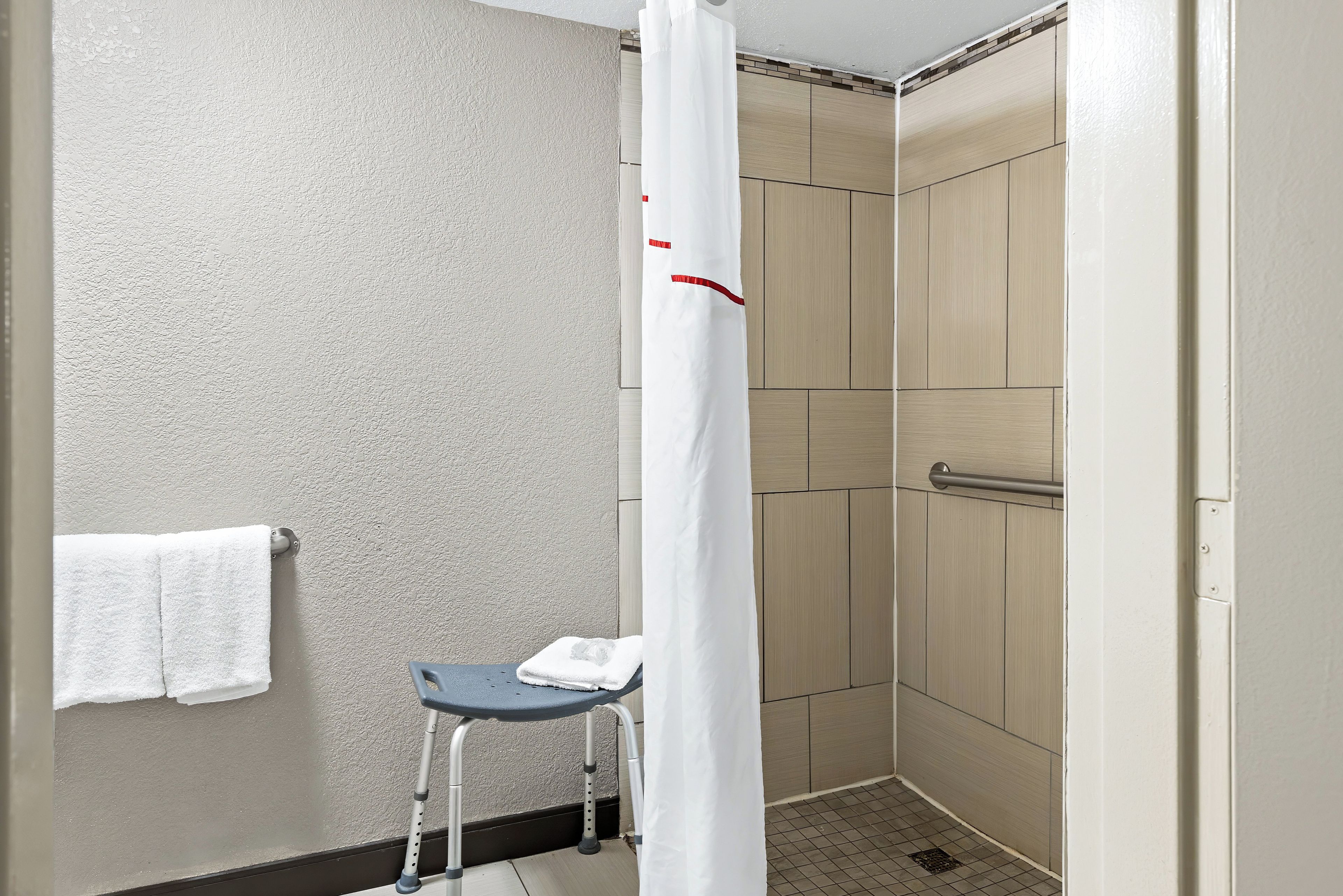 A bathroom with a shower, a towel rack, and a wheelchair.