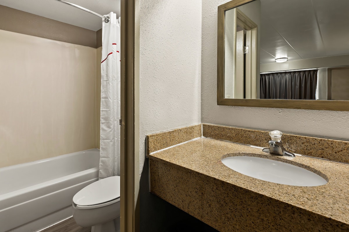 A bathroom with a white toilet, a sink with a granite countertop, and a shower curtain.