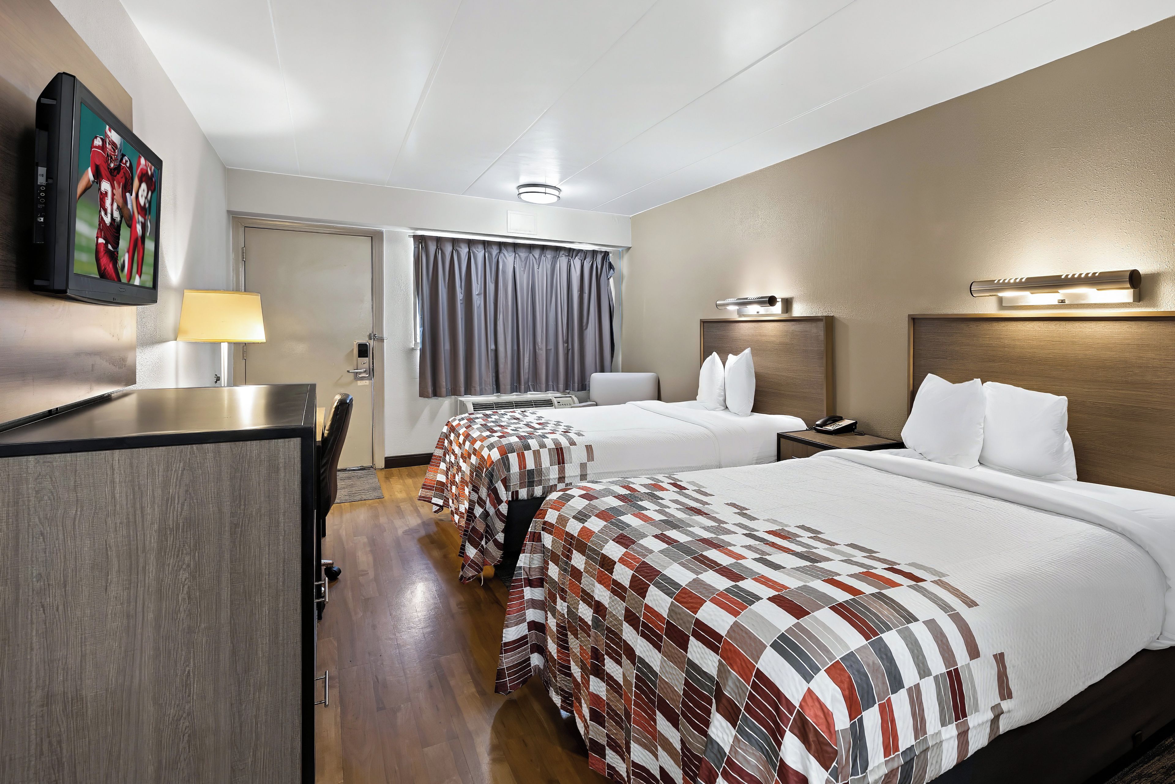 A hotel room with two beds, a desk, a television, and a lamp.