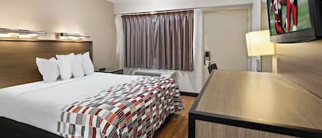 Une chambre d’hôtel avec un grand lit, un bureau, une télévision et une fenêtre avec des rideaux.