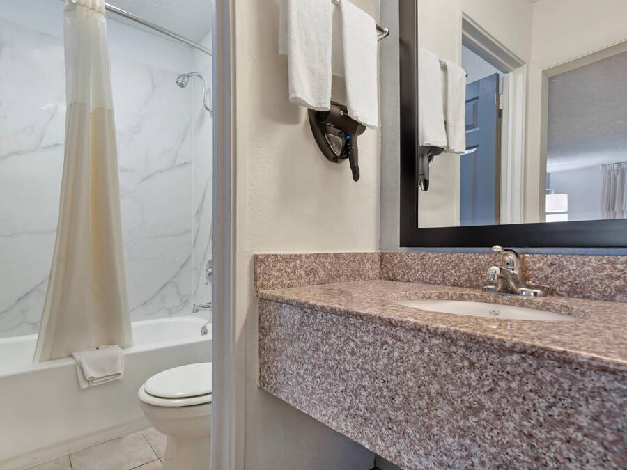 A bathroom with a marble wall, a shower curtain, a toilet, a sink with a granite countertop, and a mirror.