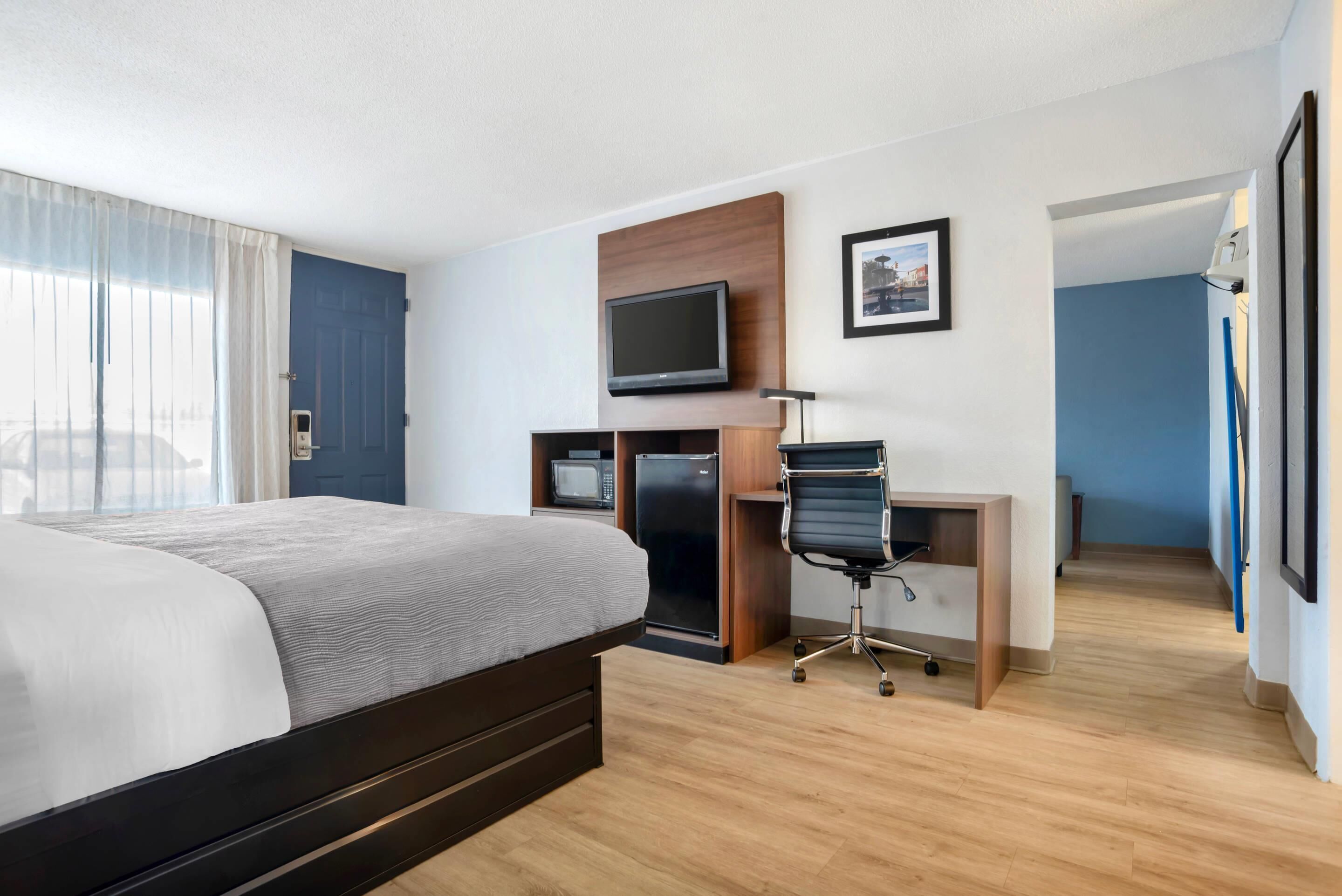 A hotel room with a bed, a desk with a computer, a television, and a microwave.