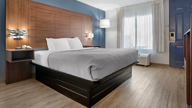 Una habitación de hotel moderna con una cama grande, cabecera de madera, lámparas de noche y una ventana con cortinas.