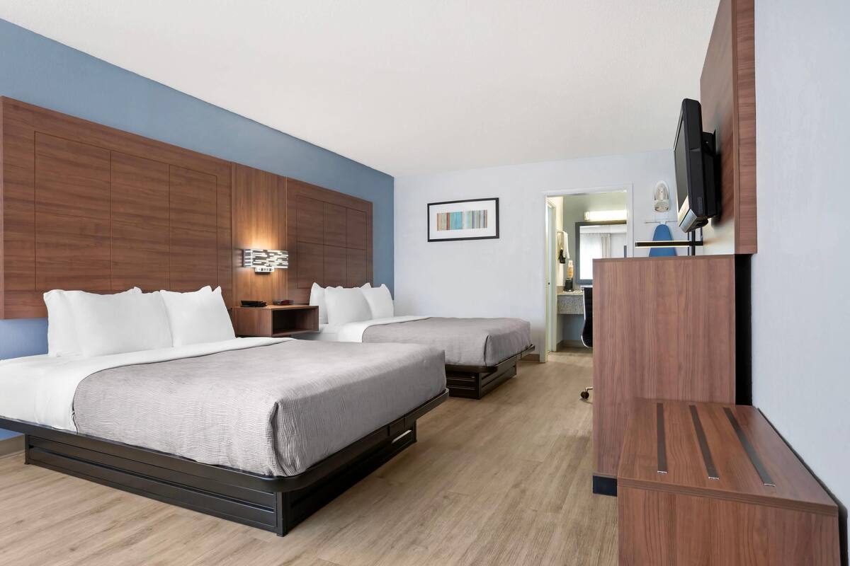 A hotel room with two beds, a wooden headboard, a flat-screen TV, and a framed picture on the wall.