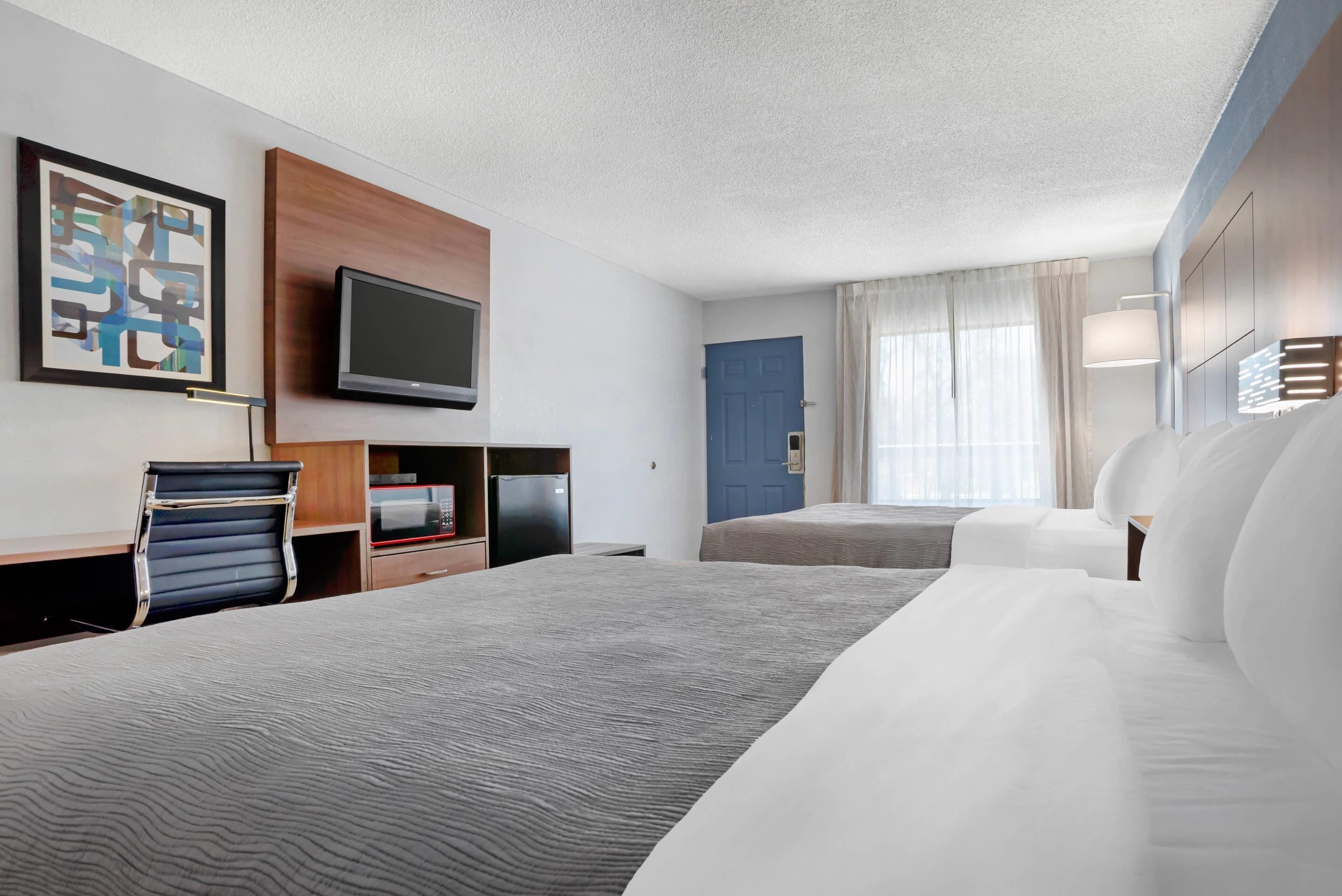 Una camera d'albergo con un letto grande, una scrivania con una sedia, una televisione e una porta blu.