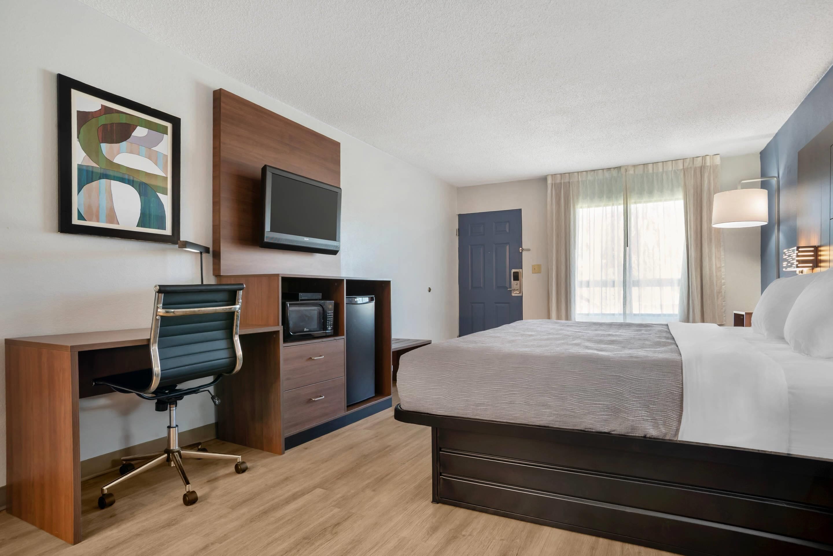 A hotel room with a bed, desk, chair, television, and artwork.