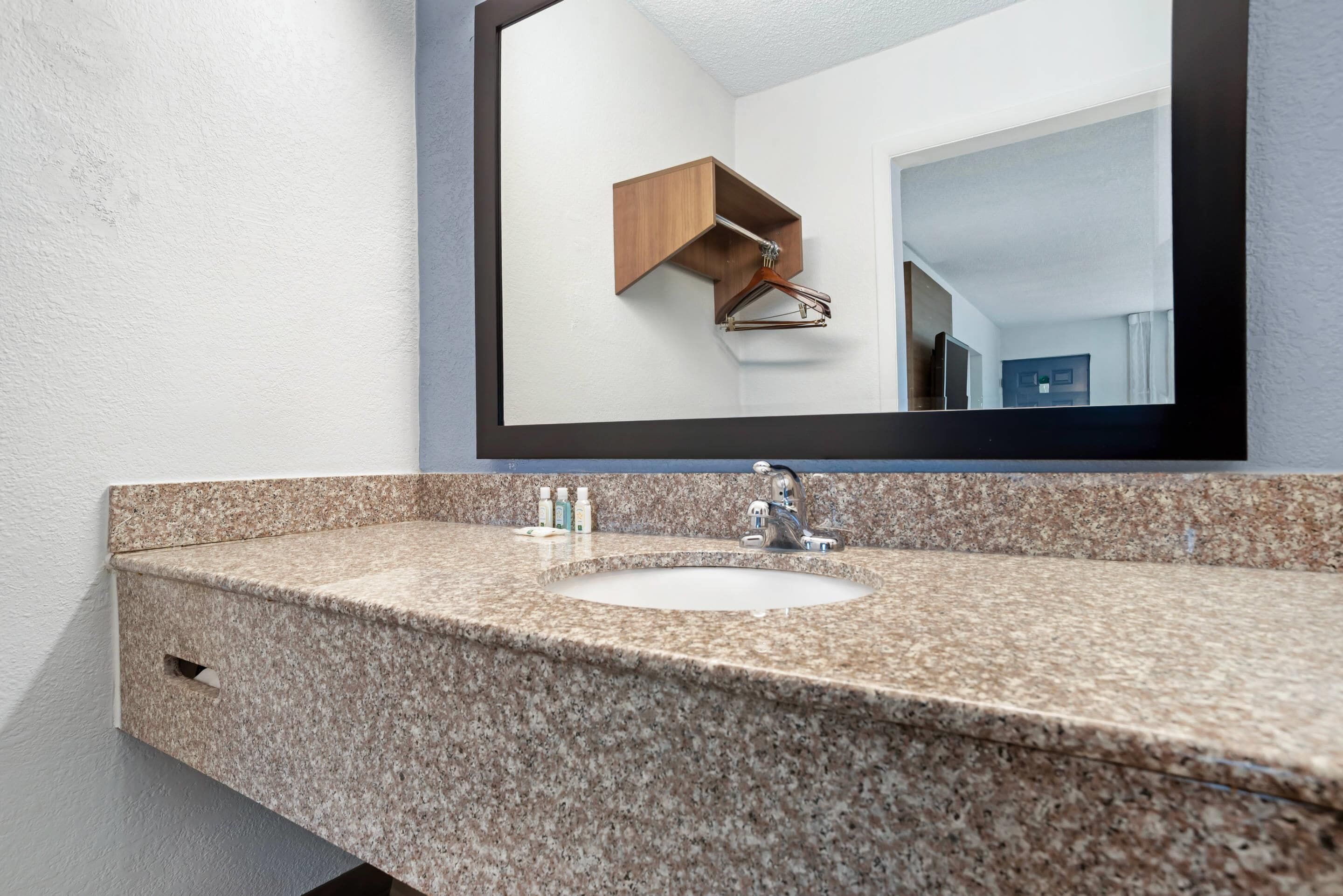 Un baño con encimera de granito, lavamanos, espejo y armario de madera.