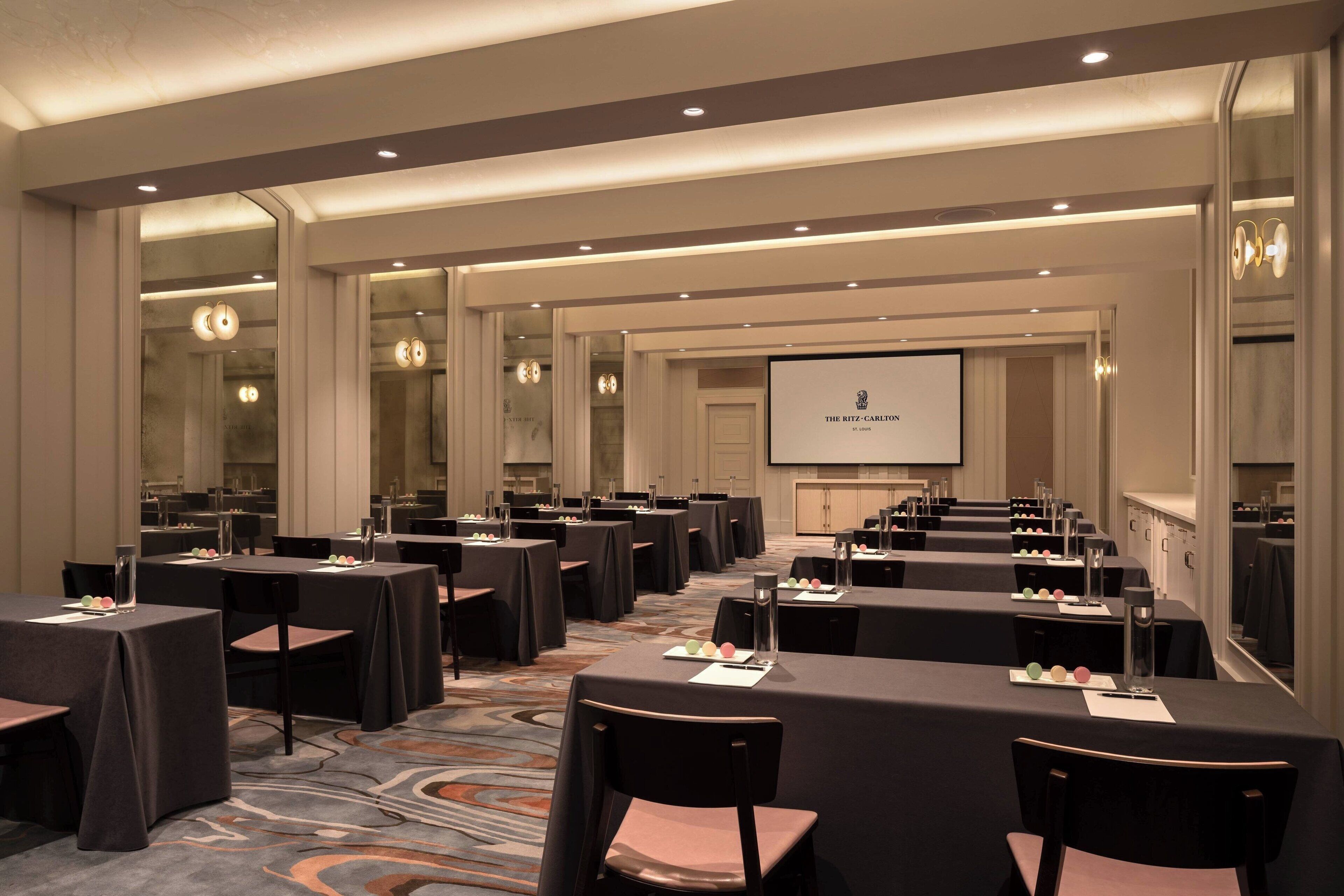 Uma sala de conferências com mesas, cadeiras e uma tela de projetor exibindo 'The Ritz-Carlton'.