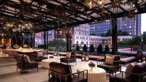 An outdoor seating area with modern furniture, a bar, and large windows offering views of a cityscape. - The Ritz-Carlton, St. Louis (St. Louis)