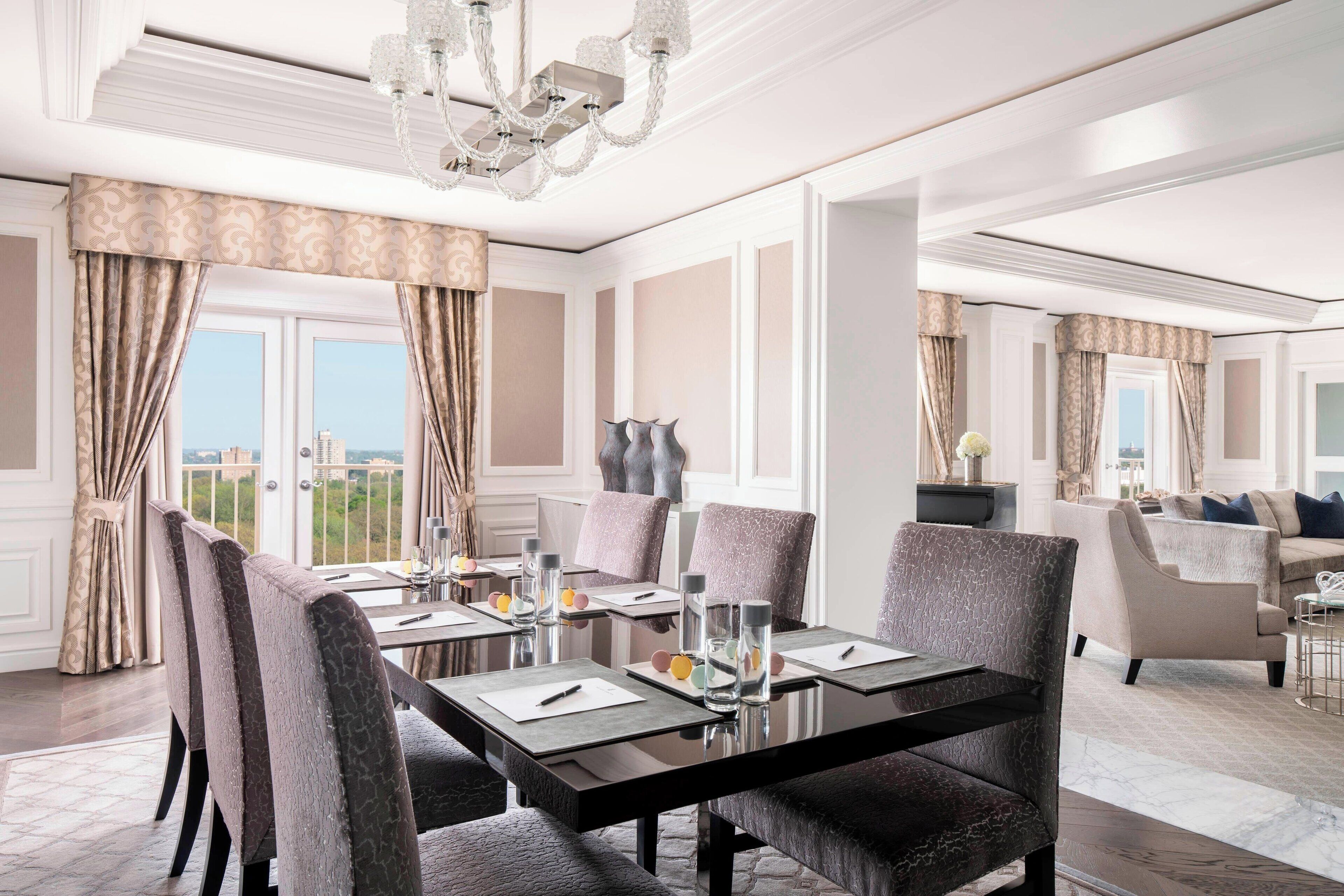 A hotel dining area with a long table set for a meal, surrounded by upholstered chairs.