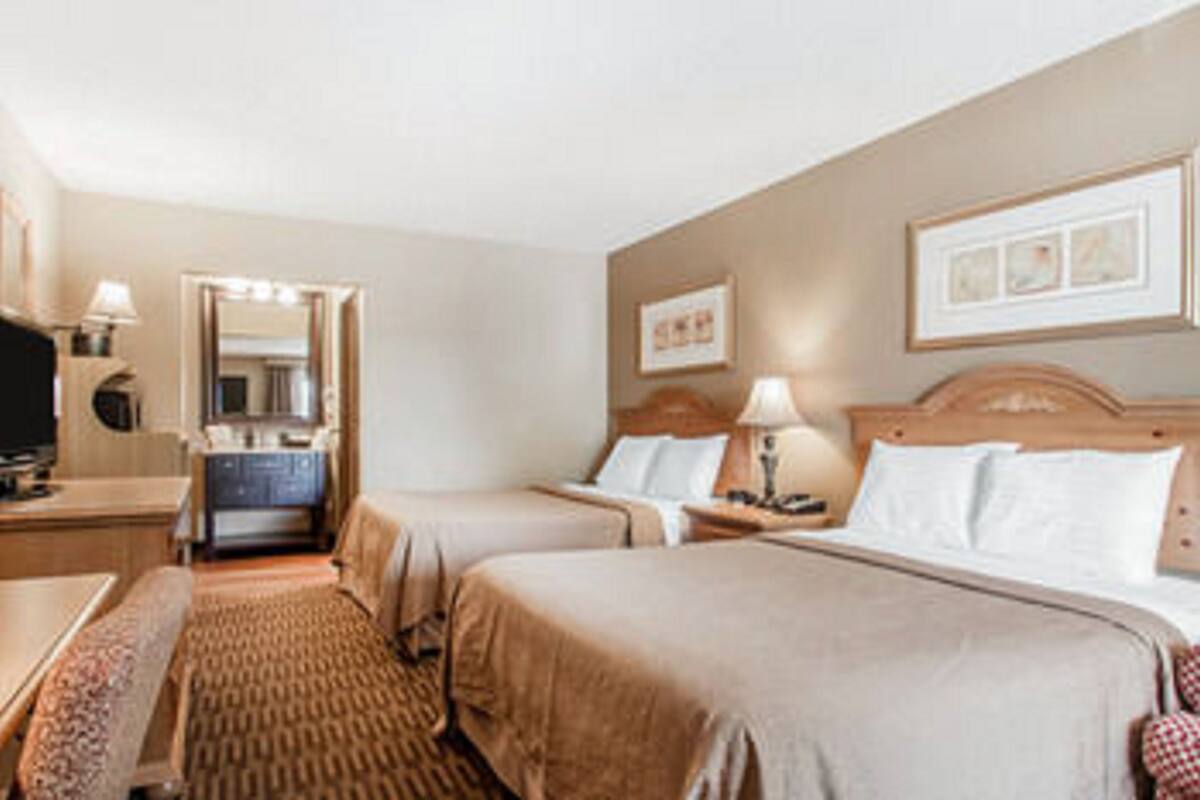 A hotel room with two beds, a desk, a mirror, and a bathroom visible through an open door.